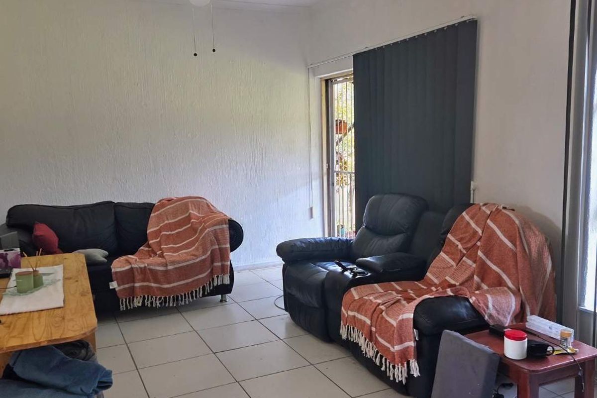 A living room featuring white tiled flooring, a ceiling fan, and vertical blinds leading to an outdoor area.