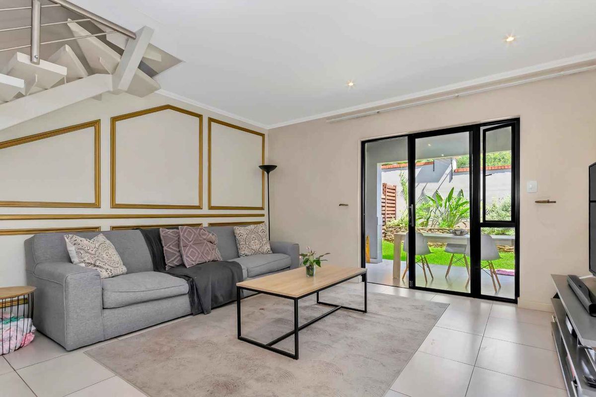 Bright living room featuring tiled flooring, decorative wall molding, and large sliding glass doors providing seamless access to the outdoor patio and garden area.