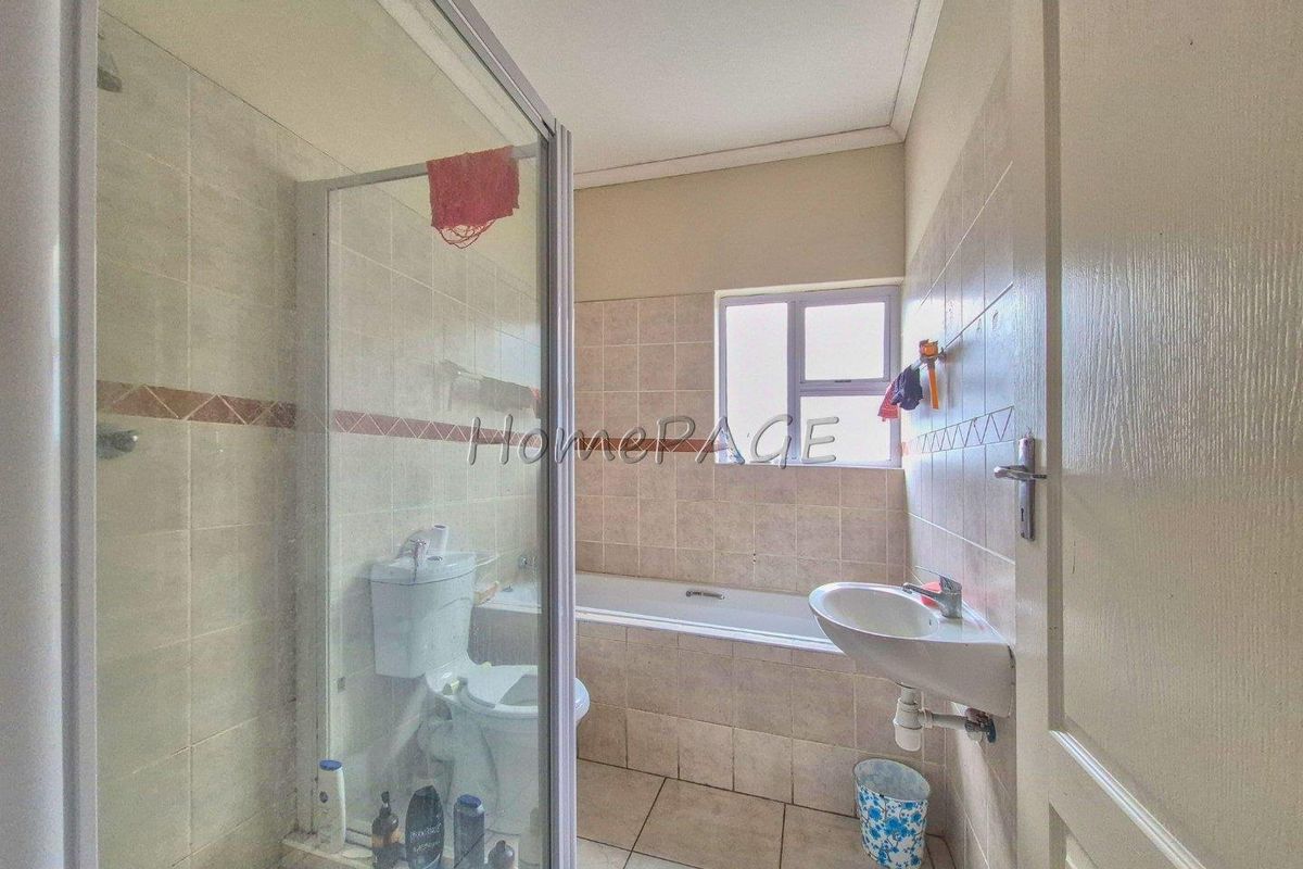 A functional bathroom featuring a glass-enclosed shower, a standard bathtub, a pedestal basin, and neutral wall tiling.