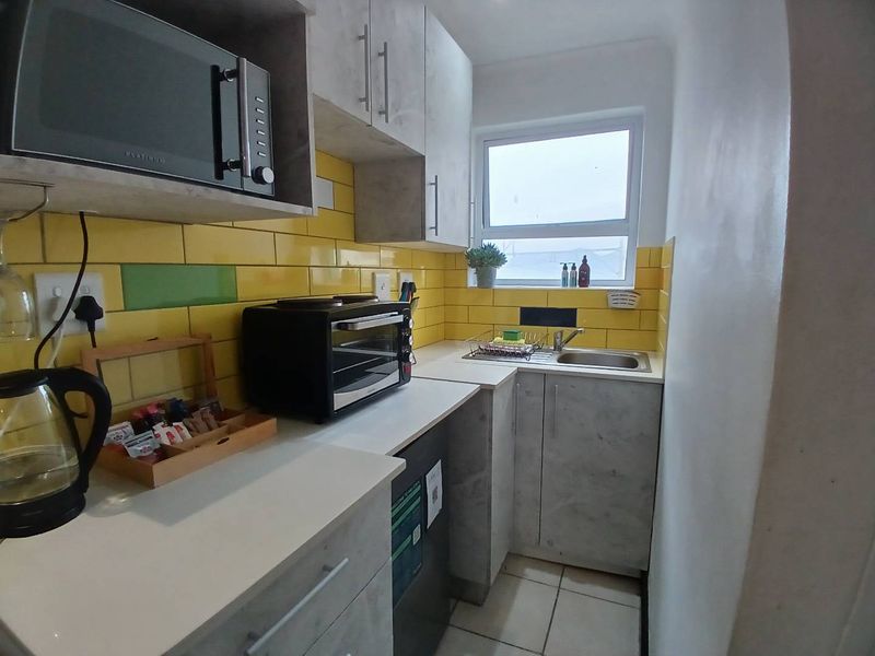 Compact kitchen featuring modern grey cabinetry, yellow tiled backsplash, stainless steel sink, and built-in microwave, offering a functional and efficient workspace.