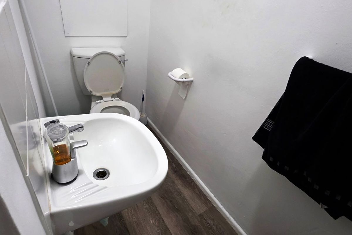 A compact office restroom featuring a white ceramic toilet, a wall-mounted basin with chrome faucet, and wood-look vinyl flooring.