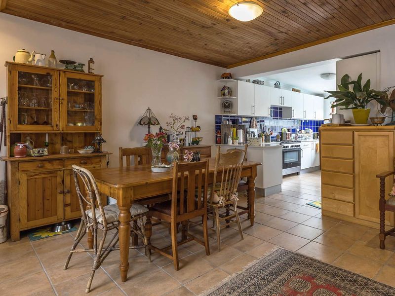 Open plan dining area featuring timber ceiling and tiled flooring, flowing into a functional kitchen with white cabinetry and blue tiled splashback.