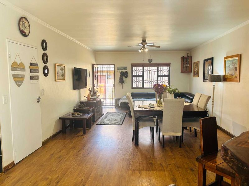 Spacious open-plan living and dining area featuring laminate flooring, a ceiling fan, and secure window bars, providing a functional and well-lit communal space.