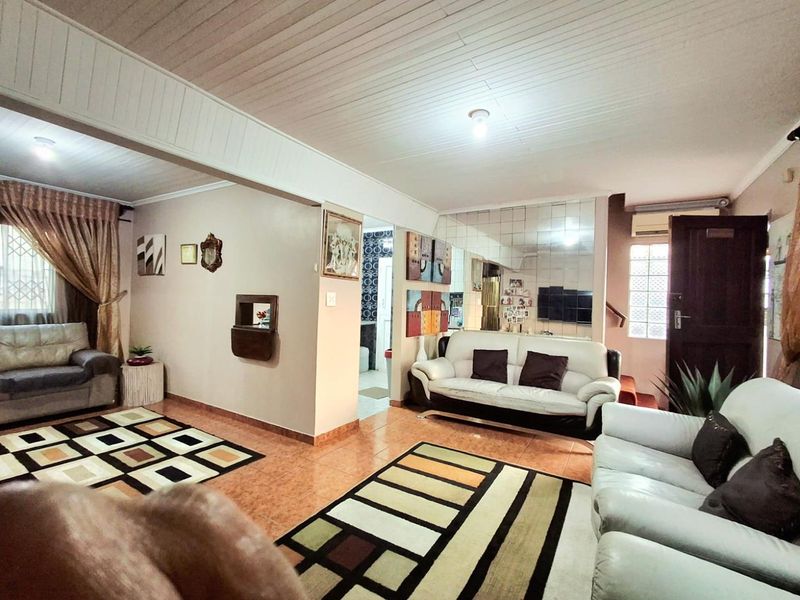 Spacious living area featuring tiled flooring, a timber ceiling, and a decorative mirrored wall panel, offering a functional layout with potential for modernization.