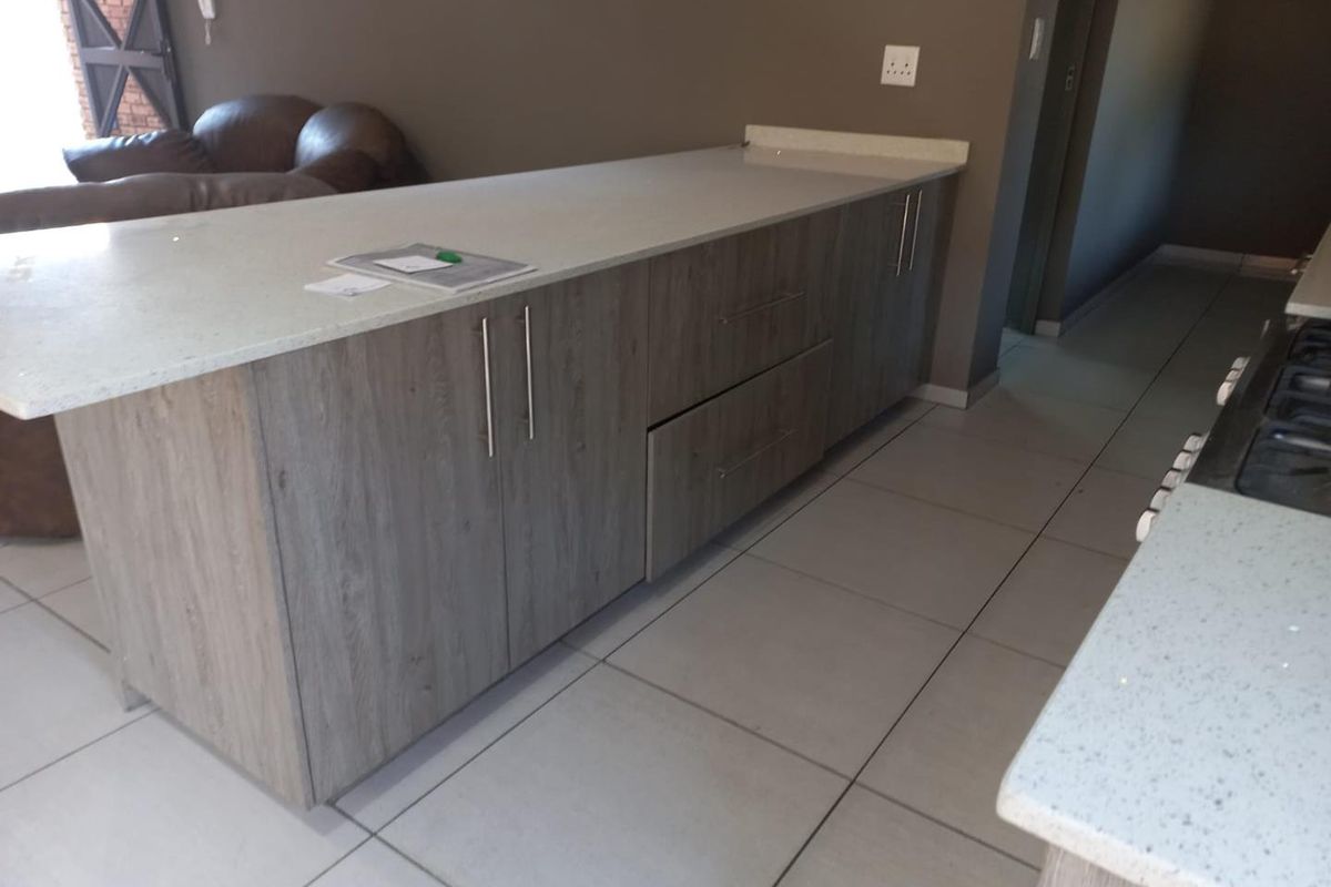 Modern kitchen featuring stone countertops, wood-look laminate cabinetry, and neutral ceramic floor tiles with an integrated gas hob.