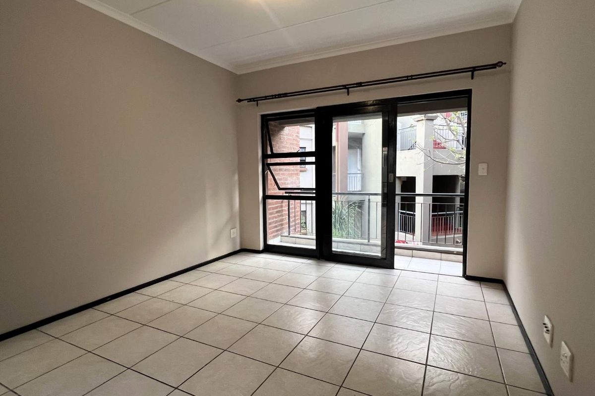 A bright, empty bedroom featuring tiled flooring and large sliding glass doors that open onto a private balcony.
