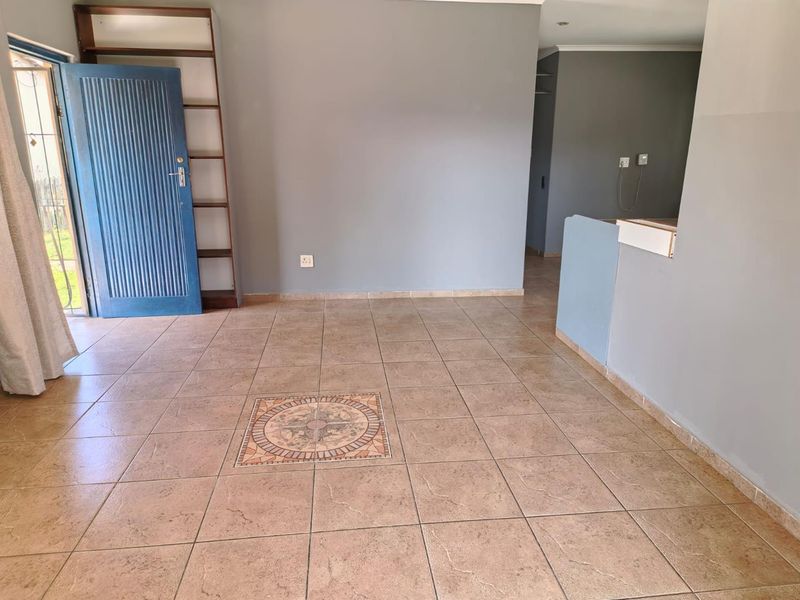 An open-plan living area featuring neutral grey walls, tiled flooring with a decorative inlay, and a built-in shelving unit.
