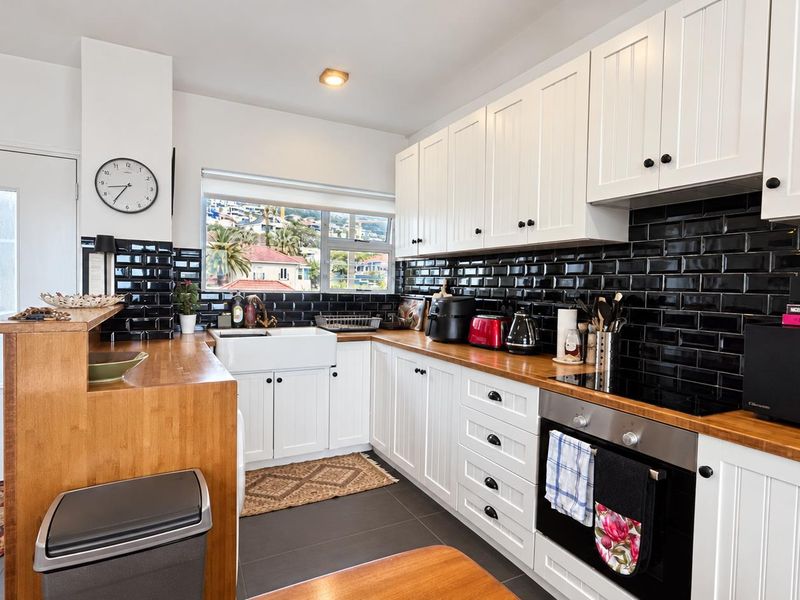 A well-maintained kitchen featuring white shaker cabinetry, butcher block countertops, a classic farmhouse sink, and a striking black subway tile backsplash.