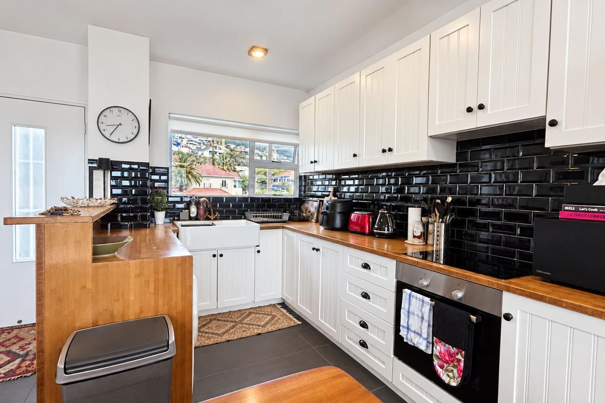 A well-maintained kitchen featuring white shaker cabinetry, butcher block countertops, a classic farmhouse sink, and a striking black subway tile backsplash.