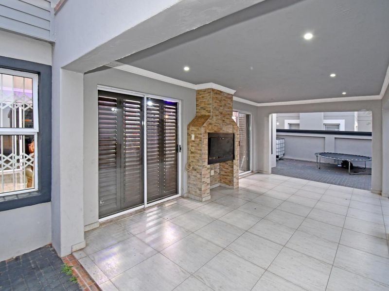 A spacious covered patio featuring tiled flooring, recessed lighting, and a built-in fireplace, providing an ideal area for outdoor entertaining.
