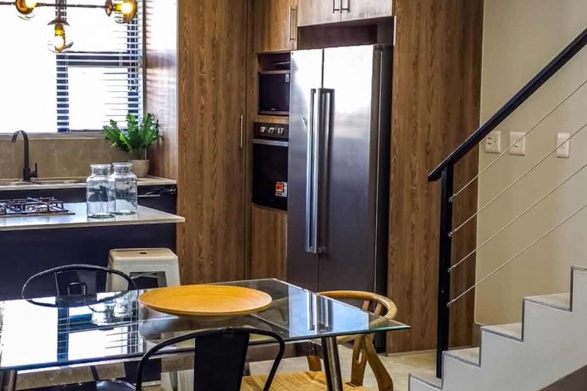 Modern open-plan kitchen and dining area featuring wood-grain cabinetry, integrated appliances, and a staircase with a contemporary metal railing.
