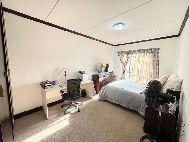 A functional bedroom featuring neutral carpet flooring, a ceiling light fixture, and a window with curtain tracks, providing a comfortable living space.