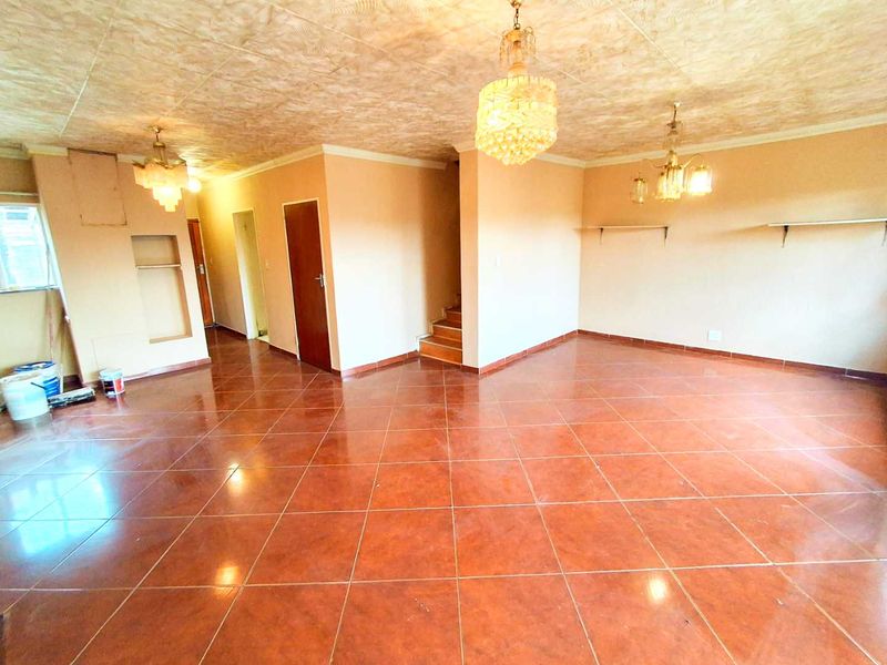 Spacious, empty living area featuring tiled flooring, a staircase, and multiple ceiling light fixtures, offering a blank canvas for renovation.