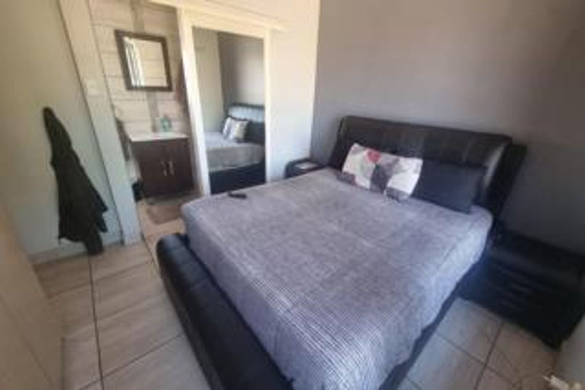 A bedroom featuring tiled flooring and an en-suite bathroom area with a vanity and mirror.