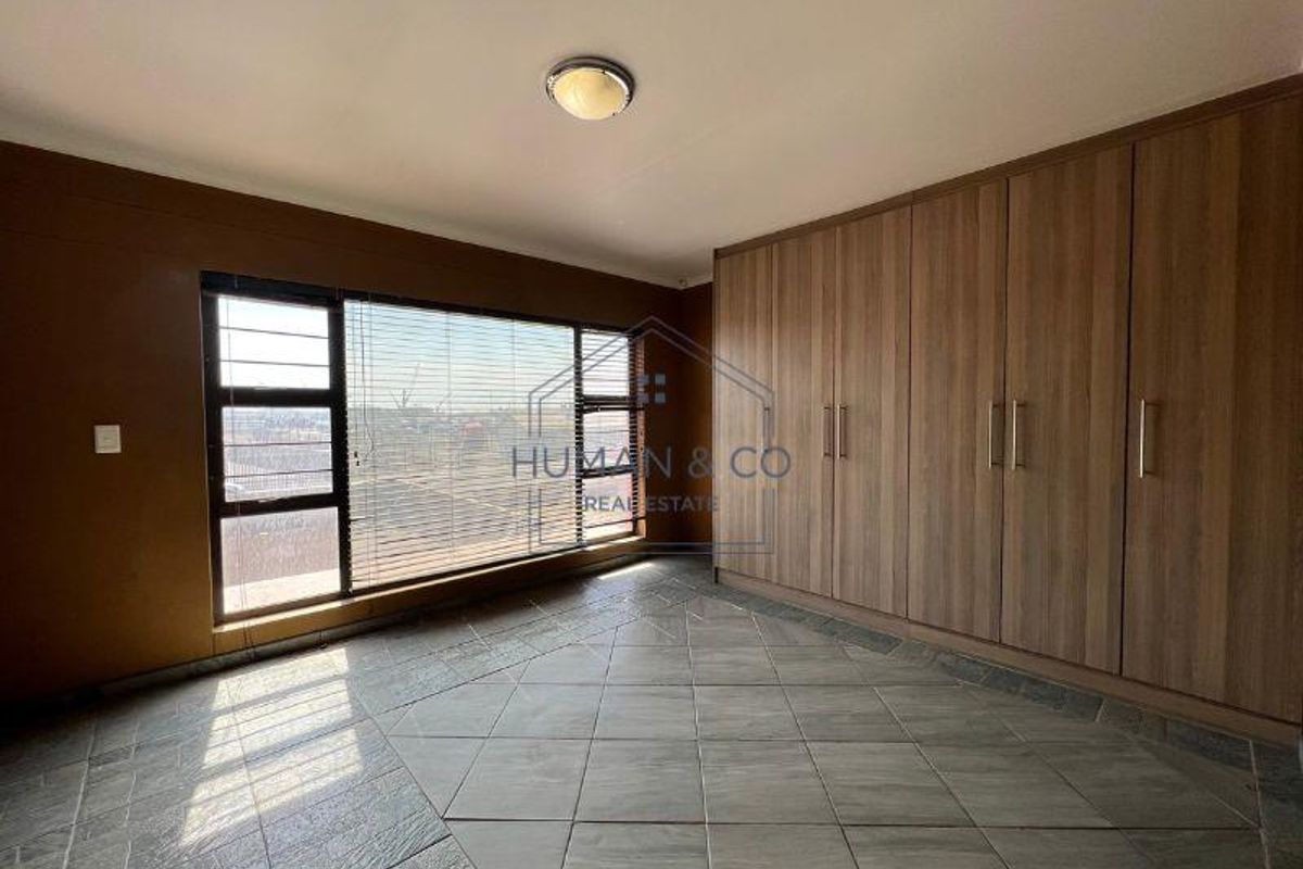 A bedroom featuring large windows with blinds, tiled flooring, and extensive built-in wooden cabinetry providing ample storage space.