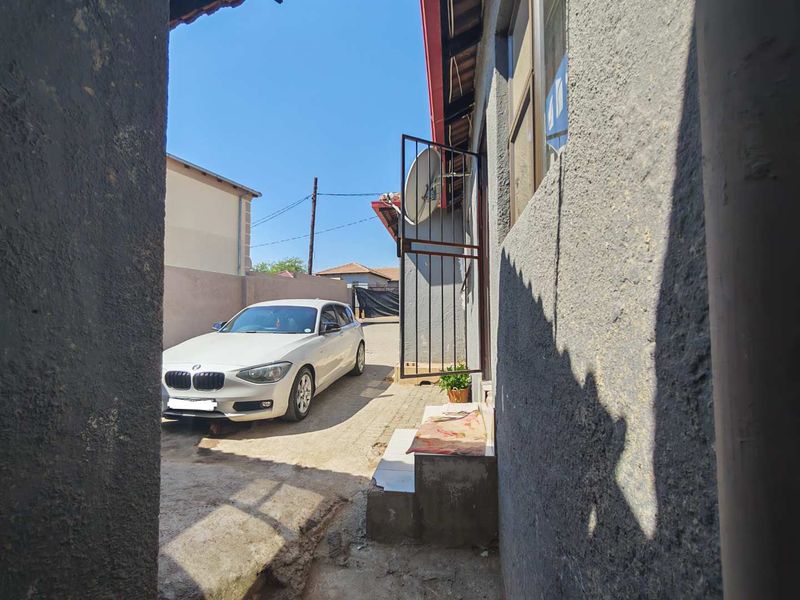A view of the rear exterior area featuring a paved driveway, boundary wall, and security gate access to the property.
