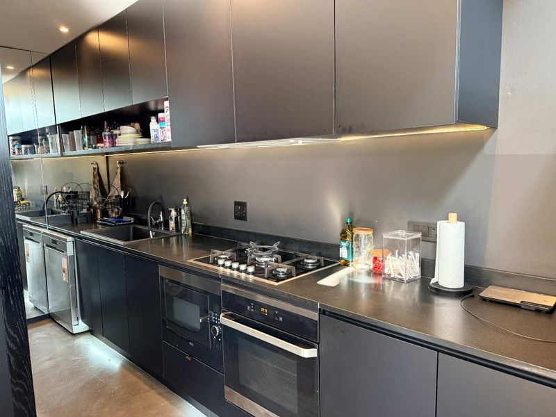 Modern kitchen featuring sleek black cabinetry, integrated appliances, a gas hob, and under-cabinet lighting, providing a contemporary and functional workspace.