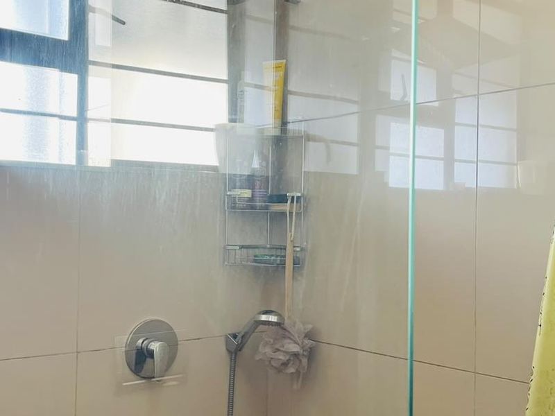 A functional shower enclosure featuring a modern rain shower head, handheld attachment, and glass screen with neutral wall tiling.