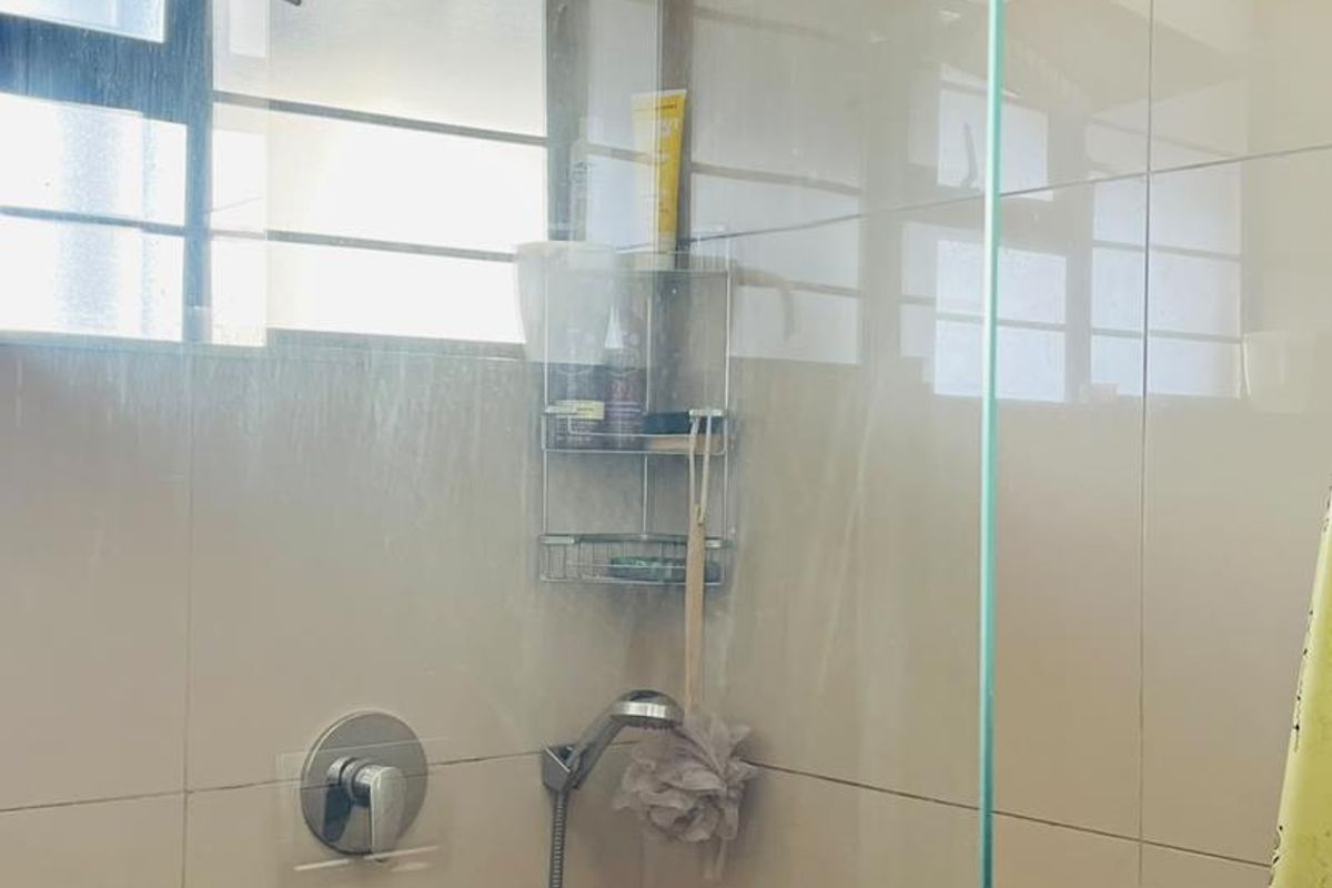 A functional shower enclosure featuring a modern rain shower head, handheld attachment, and glass screen with neutral wall tiling.