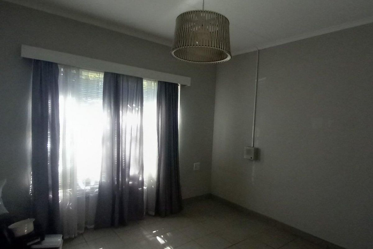 A vacant bedroom featuring tiled flooring and natural light through a window with curtain tracks installed.