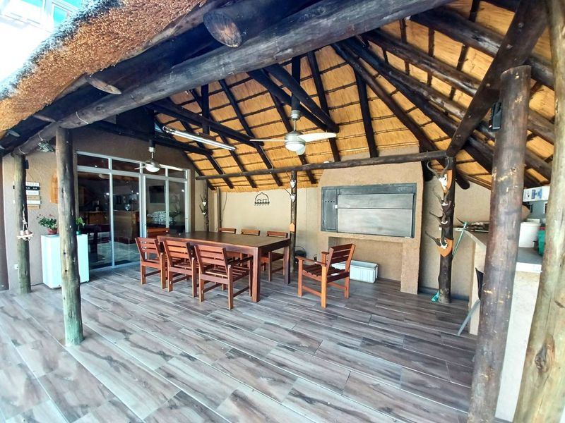 Spacious covered patio featuring a traditional thatched roof, exposed timber beams, built-in braai, and modern tiled flooring, perfect for outdoor entertaining.