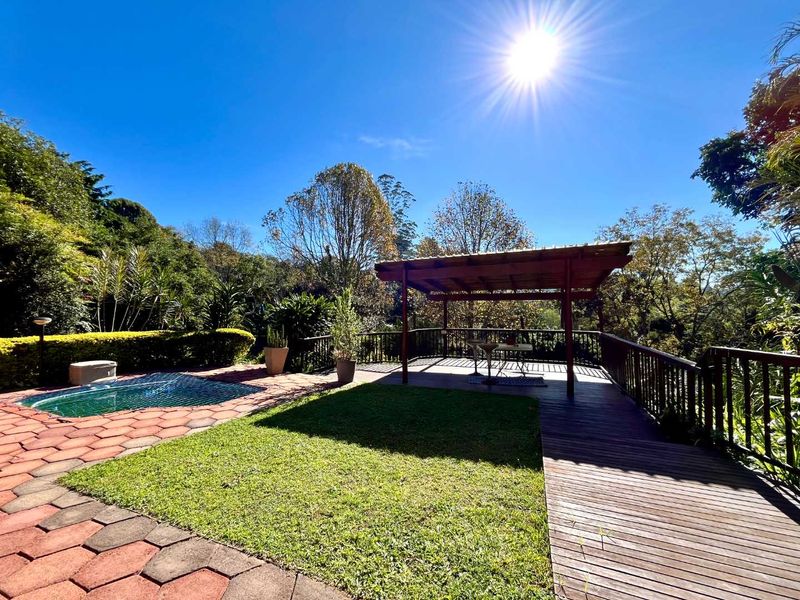 Outdoor entertainment area featuring a swimming pool, a timber pergola, and a spacious wooden deck surrounded by landscaped garden.