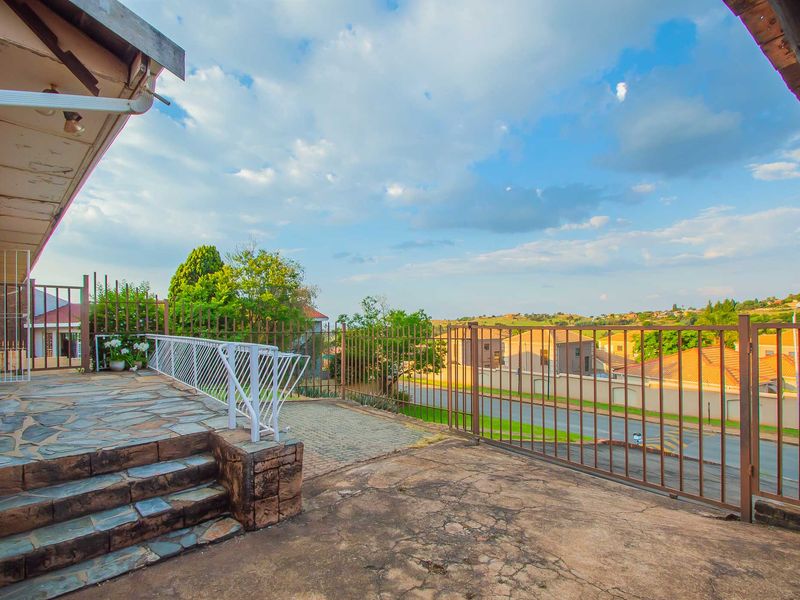 An elevated outdoor patio area featuring stone paving, metal security fencing, and steps, offering an open view of the surrounding residential neighbourhood.