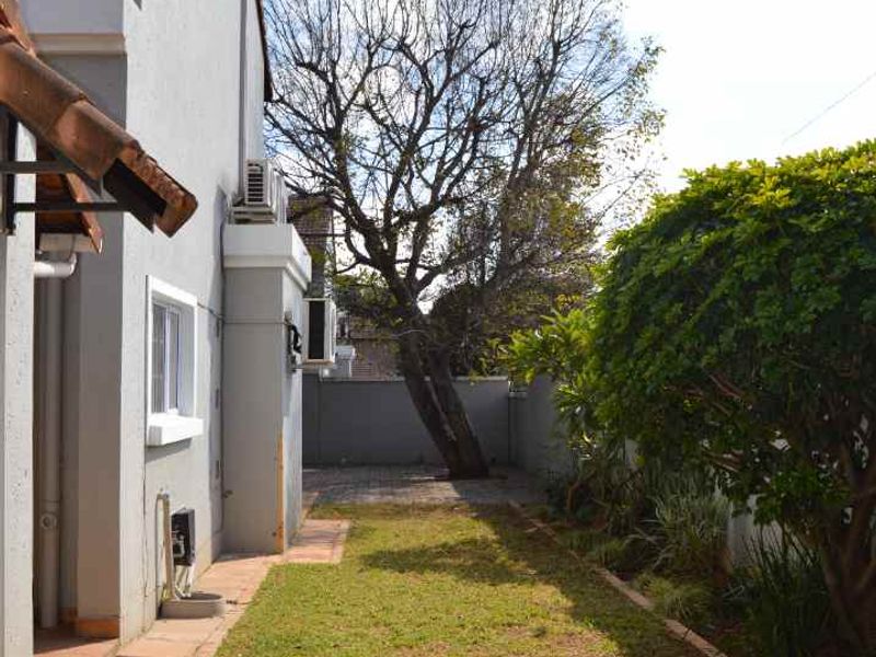 A side garden area featuring a paved walkway, lawn, and boundary wall, providing access along the side of the property.