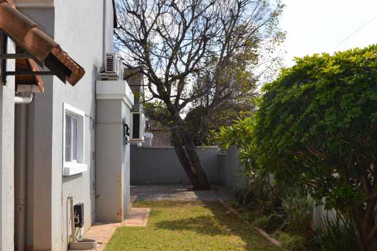 A side garden area featuring a paved walkway, lawn, and boundary wall, providing access along the side of the property.
