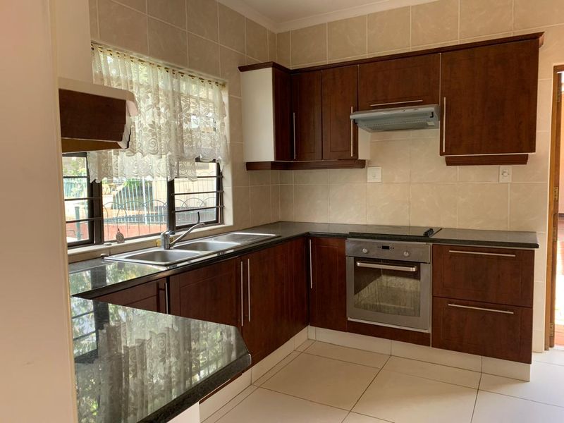 A functional kitchen featuring dark wood cabinetry, granite countertops, built-in oven, electric hob, and tiled finishes throughout.