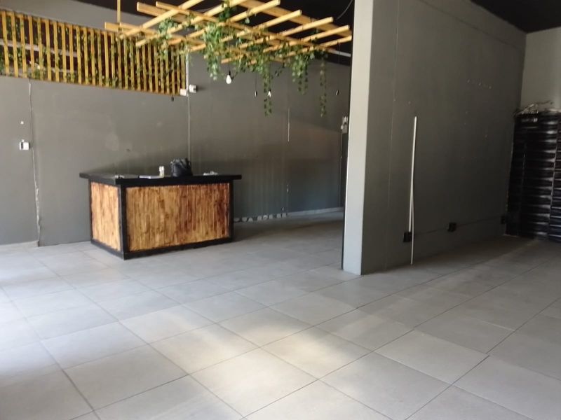 Open plan retail space featuring large format floor tiles, a built-in service counter, and a decorative suspended timber ceiling element.