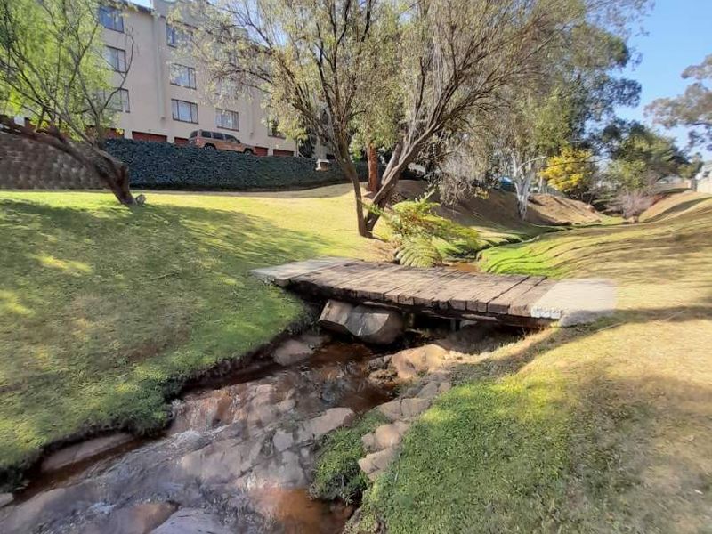 A scenic view of a landscaped garden area featuring a natural stone-lined stream and a rustic wooden footbridge.