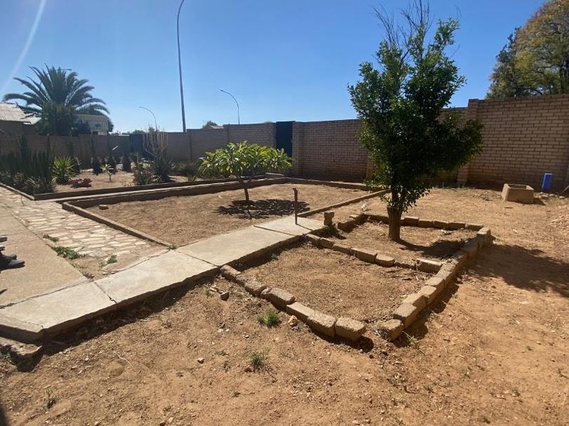 A spacious outdoor garden area featuring brick boundary walls, paved walkways, and established garden beds ready for landscaping.