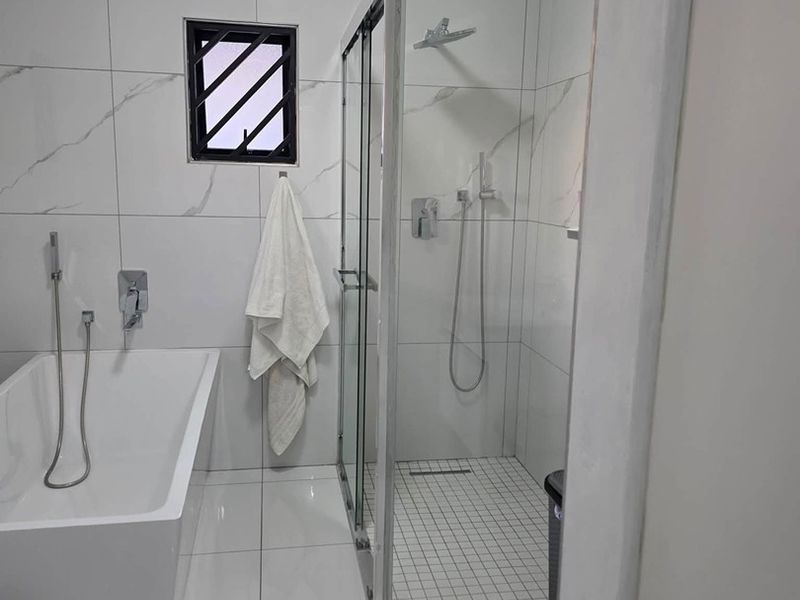 Modern bathroom featuring a sleek freestanding bathtub, a separate glass-enclosed shower, and contemporary white marble-look wall tiling.