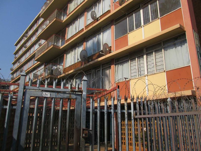 Exterior view of a multi-story apartment building featuring metal security fencing with razor wire and private balconies for each unit.