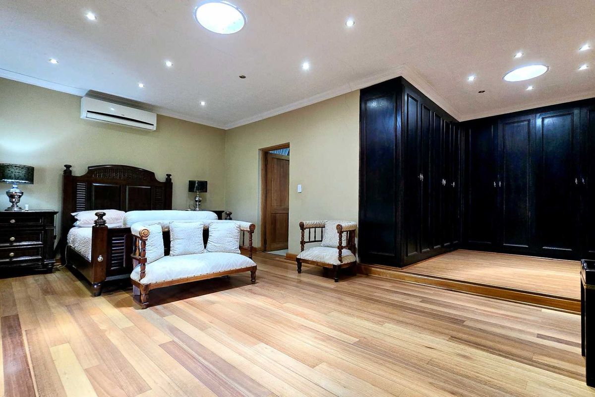 Spacious bedroom featuring polished timber flooring, recessed ceiling lighting, skylights, a wall-mounted air conditioning unit, and extensive built-in dark cabinetry.