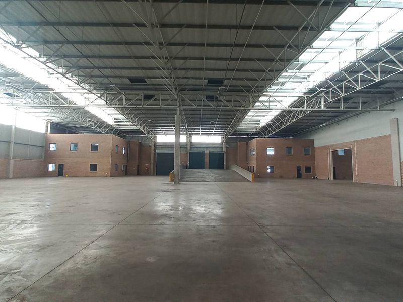 Spacious industrial warehouse featuring high ceilings with exposed steel trusses, concrete flooring, and a dedicated loading ramp for efficient logistics operations.