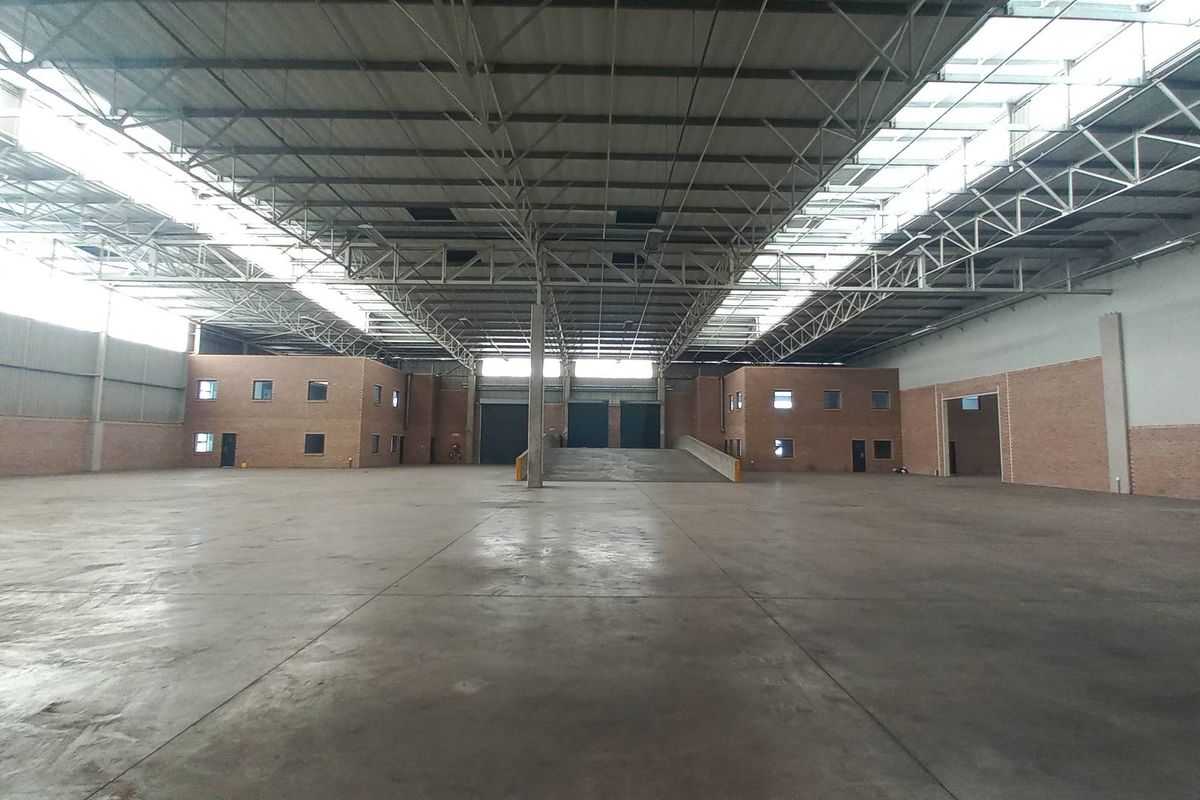 Spacious industrial warehouse featuring high ceilings with exposed steel trusses, concrete flooring, and a dedicated loading ramp for efficient logistics operations.
