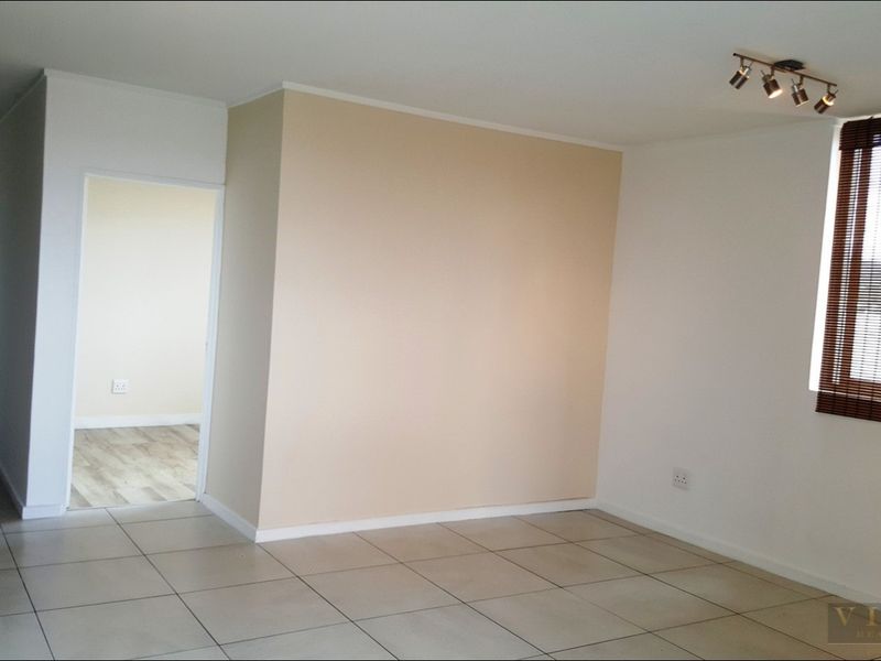 A bright, empty living area featuring neutral tiled flooring, modern track lighting, and window blinds, offering a clean and versatile space.