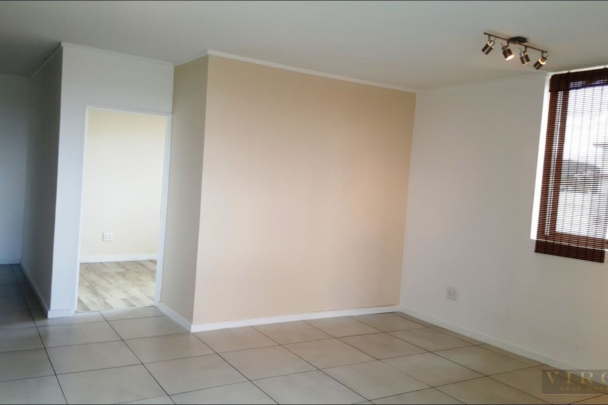 A bright, empty living area featuring neutral tiled flooring, modern track lighting, and window blinds, offering a clean and versatile space.