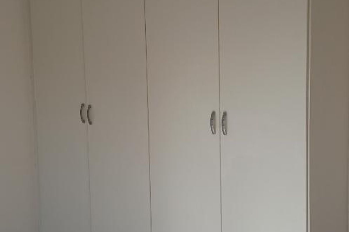 A bedroom featuring neutral tiled flooring and floor-to-ceiling built-in cupboards providing ample storage space.