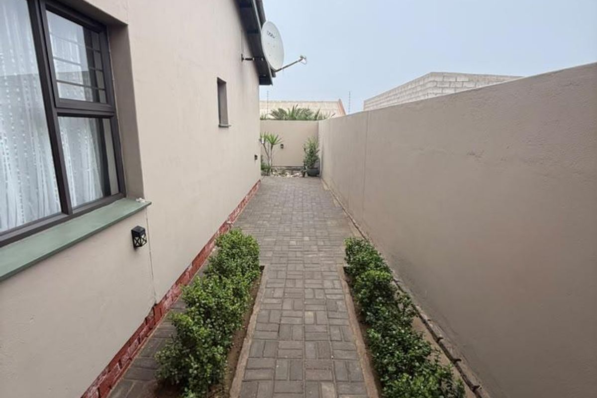 A paved side walkway featuring a boundary wall, neat garden borders, and an external wall light.