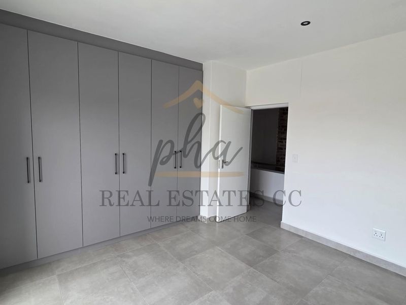 A modern, empty bedroom featuring neutral grey tiled flooring, built-in cupboards with sleek handles, and recessed ceiling lighting.