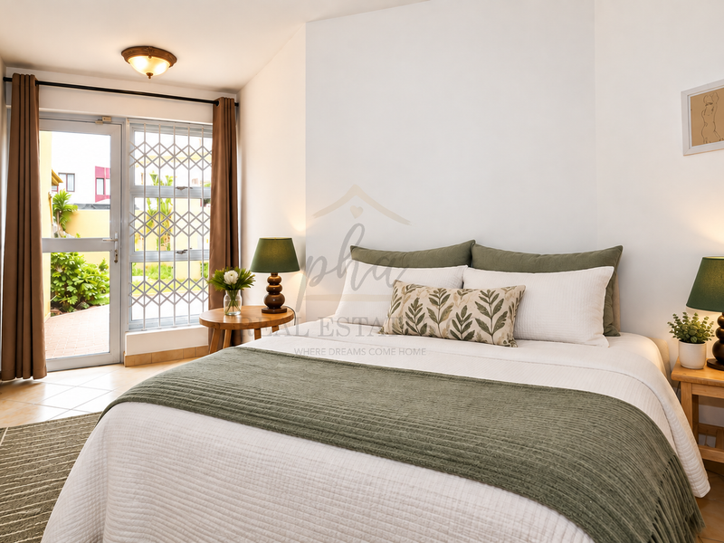 A well-lit bedroom featuring tiled flooring and a glass door with a security gate leading to an outdoor area.
