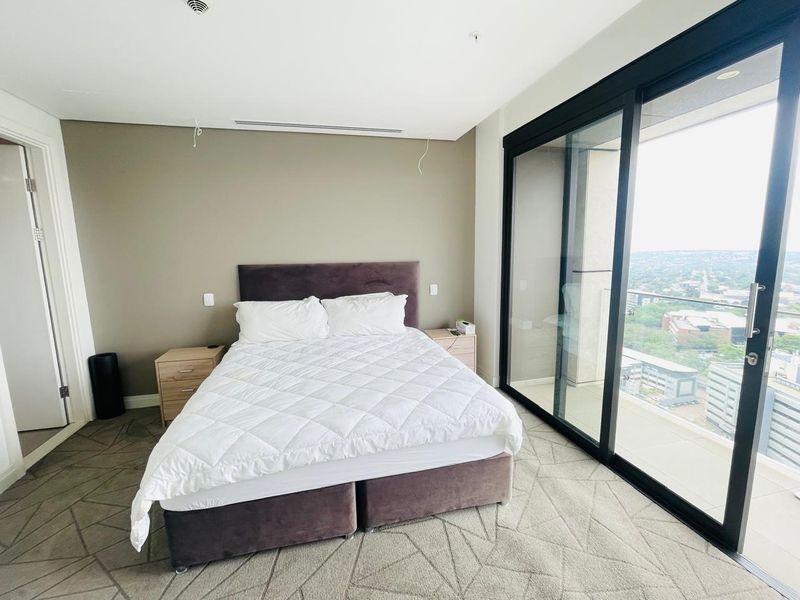 Modern bedroom featuring floor-to-ceiling sliding glass doors leading to a balcony, neutral wall tones, and integrated ceiling lighting.