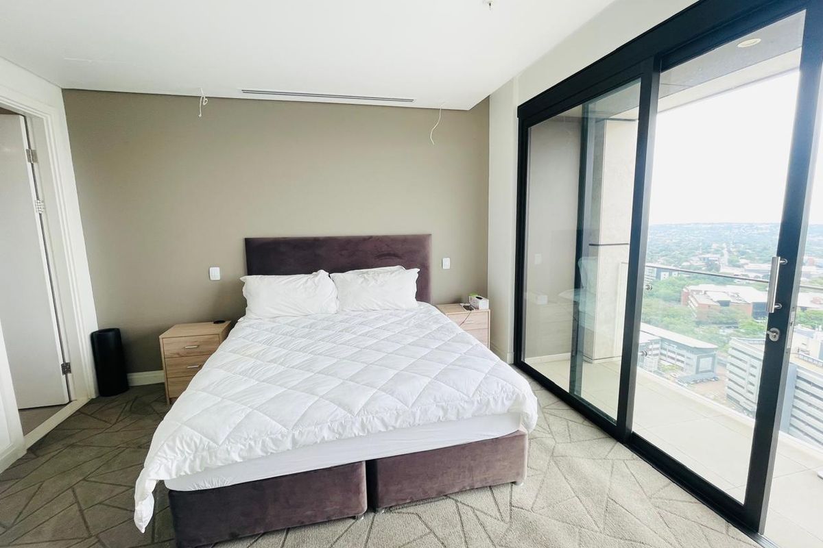 Modern bedroom featuring floor-to-ceiling sliding glass doors leading to a balcony, neutral wall tones, and integrated ceiling lighting.