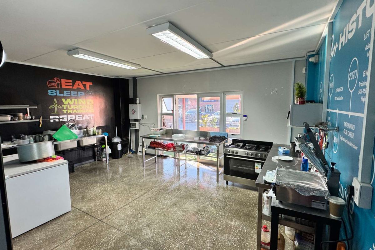 A functional commercial kitchen space featuring stainless steel prep tables, a gas stove, double sink, and polished concrete flooring.