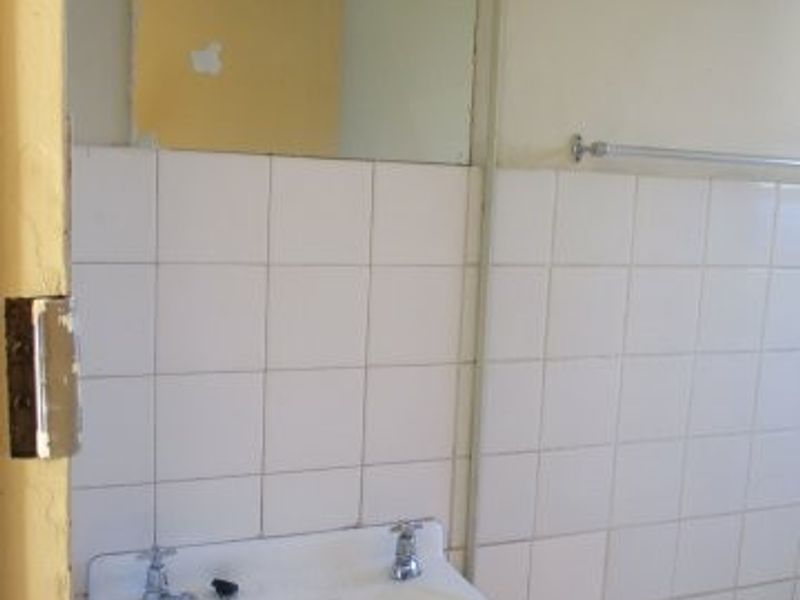 A dated bathroom featuring a wall-mounted basin, tiled splashback, and bathtub, requiring cosmetic updates and repairs to finishes.