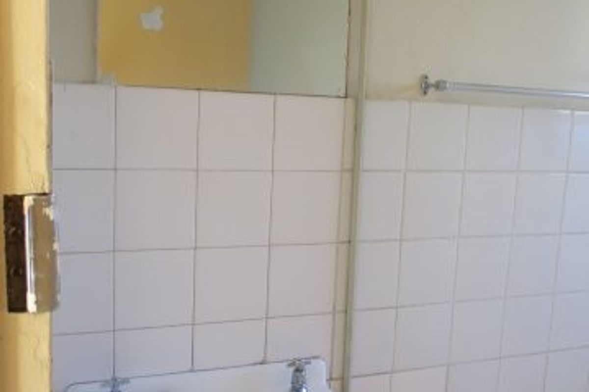 A dated bathroom featuring a wall-mounted basin, tiled splashback, and bathtub, requiring cosmetic updates and repairs to finishes.