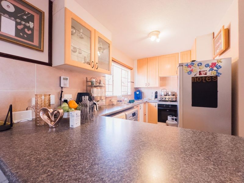 A functional kitchen featuring light wood-tone cabinetry, laminate countertops, a tiled backsplash, and integrated cooking appliances.